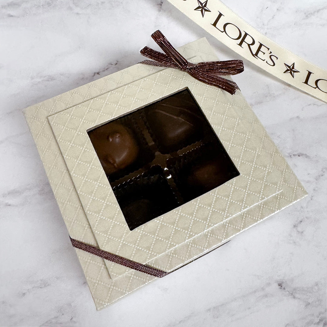 Chocolates in a decorative box with a brown ribbon on a marble surface, with 'LORE's' branding.