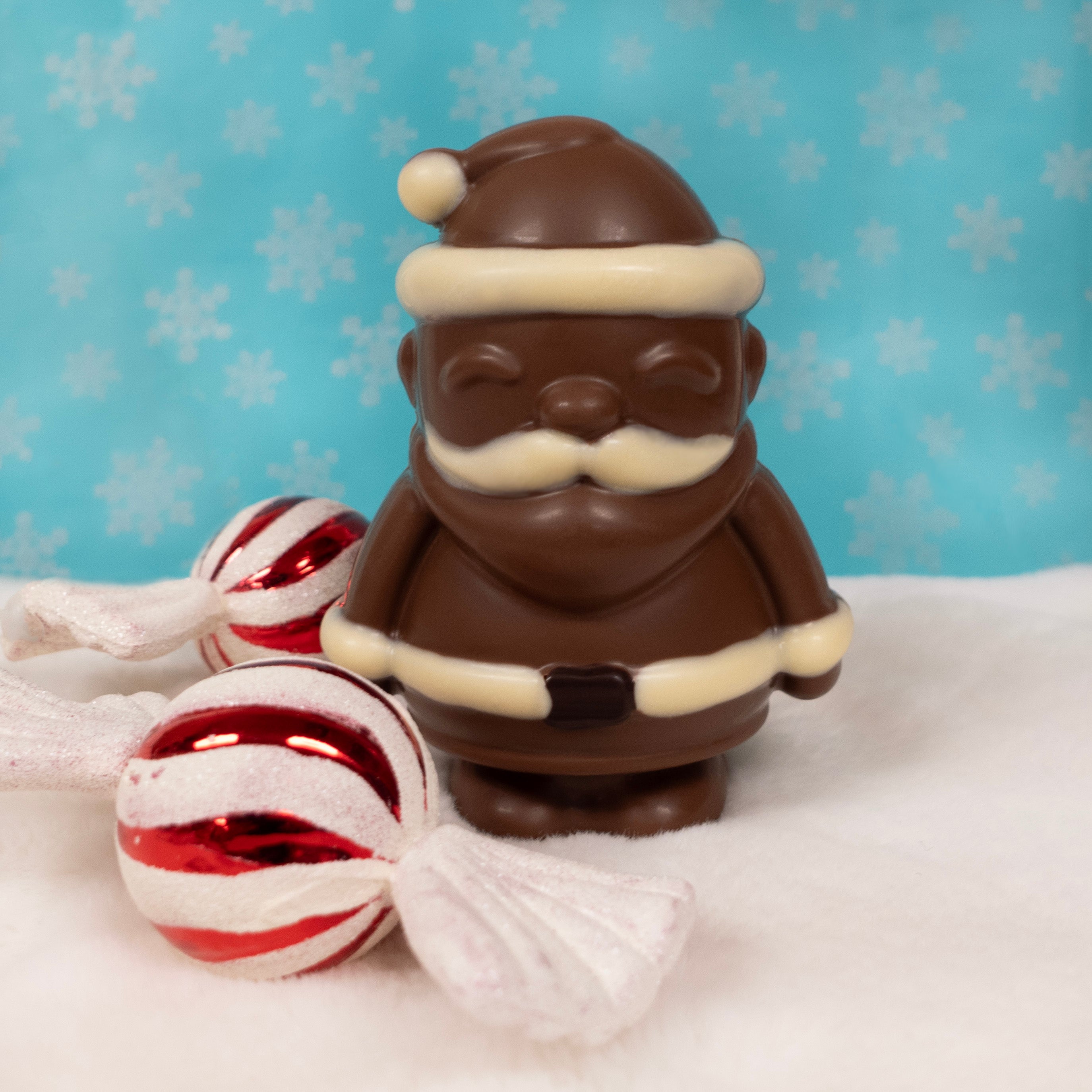 Milk Chocolate Santa Claus figurine with candy against a blue background with snowflake pattern