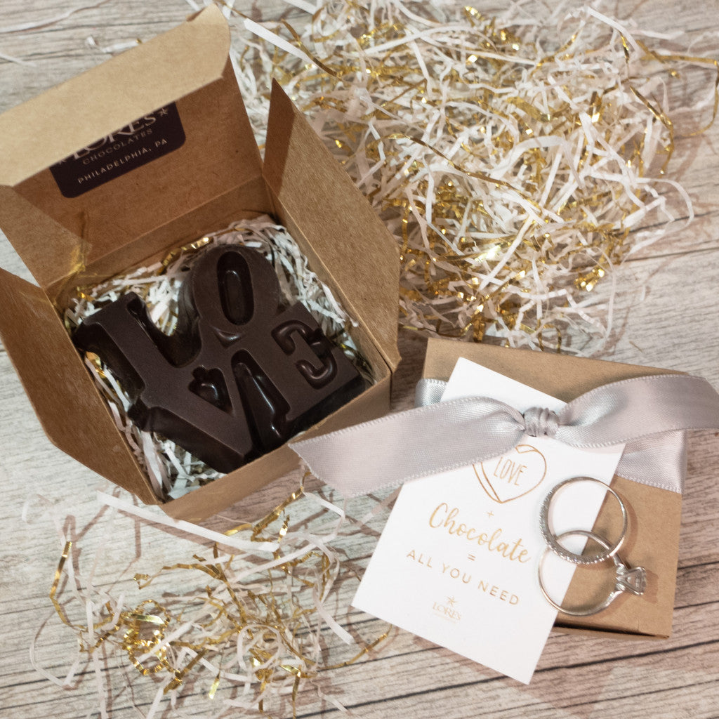 Chocolate bar with 'LOVE' letters in a gift box with a ribbon and card on a wooden surface.