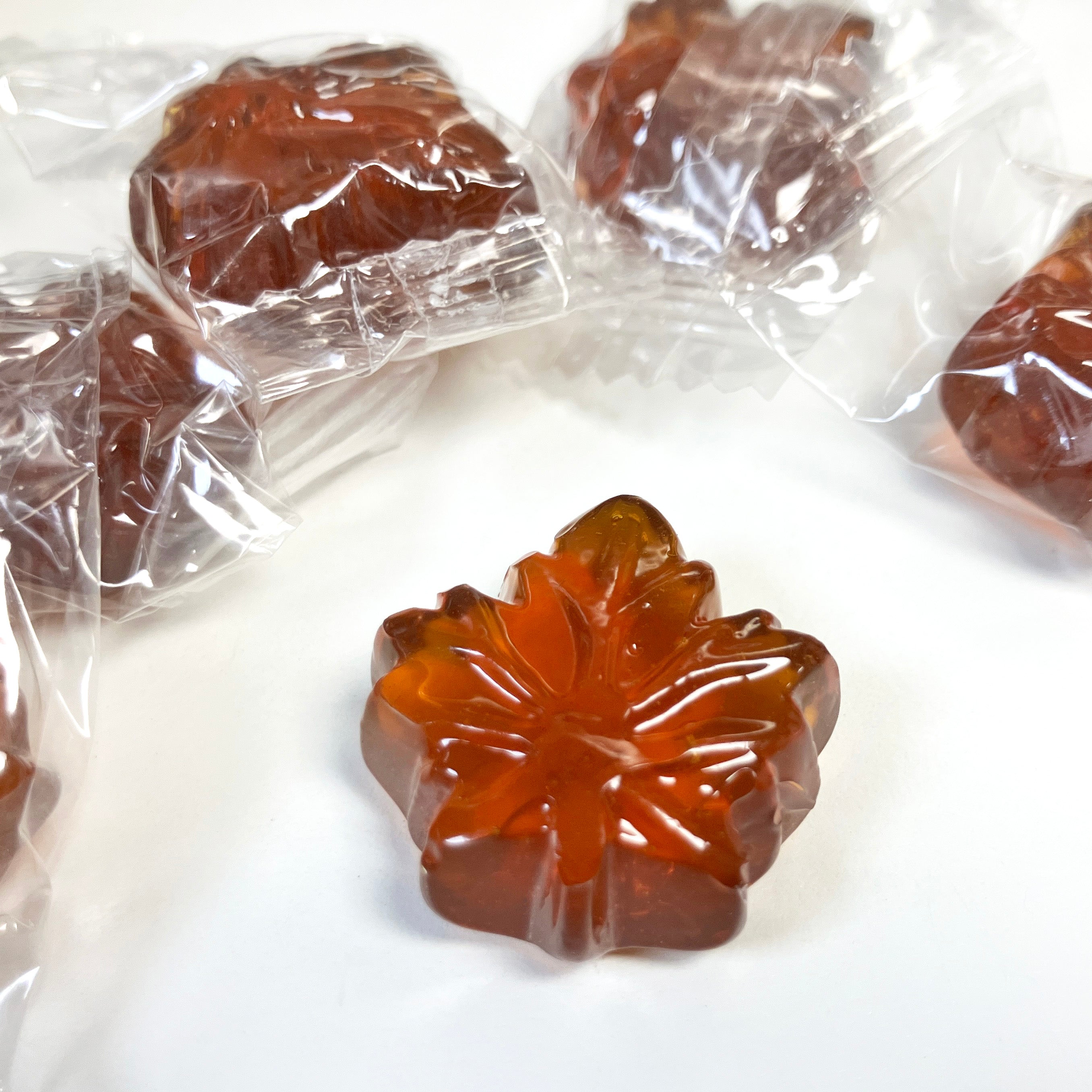 Brown hard candy with maple leaf pattern in clear plastic packaging on a white surface