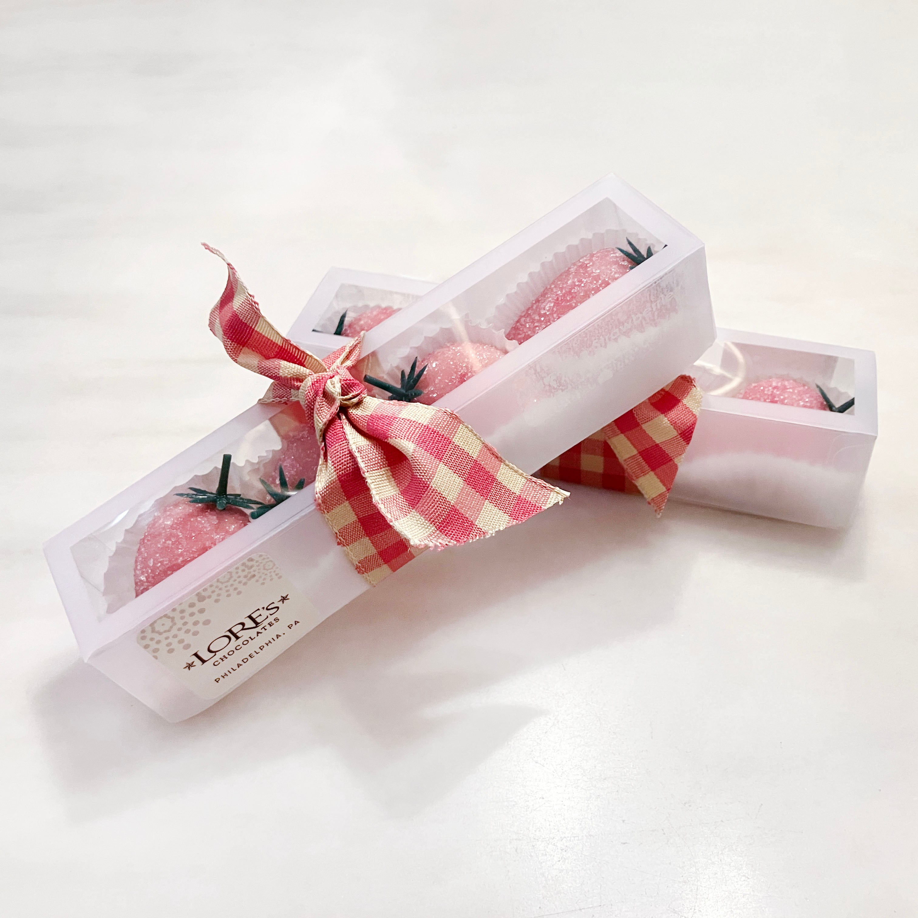Pink marzipan Strawberries in a decorative box with a checkered ribbon on a white background