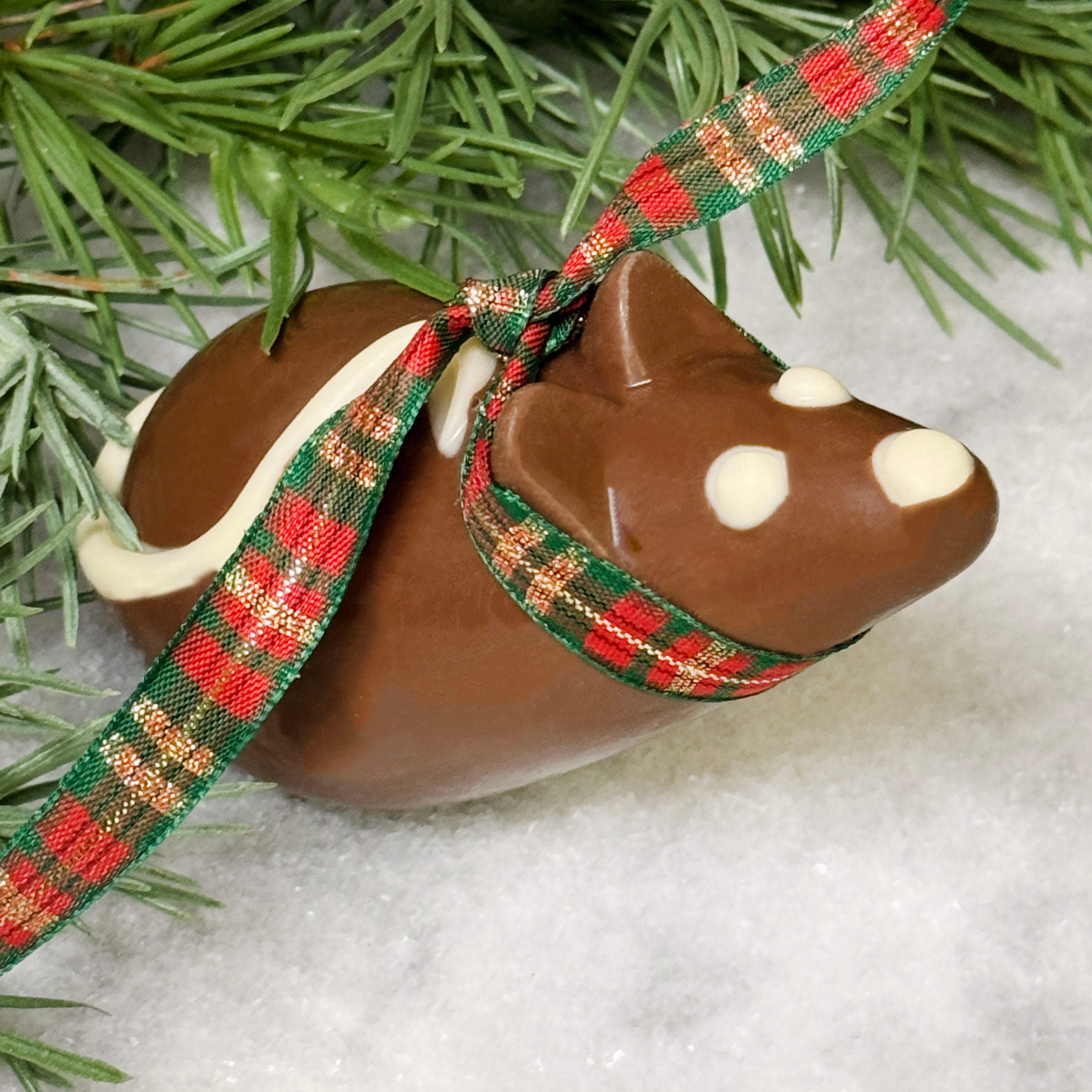Decorative milk chocolate shaped like a christmas mouse with a plaid ribbon on a snowy background