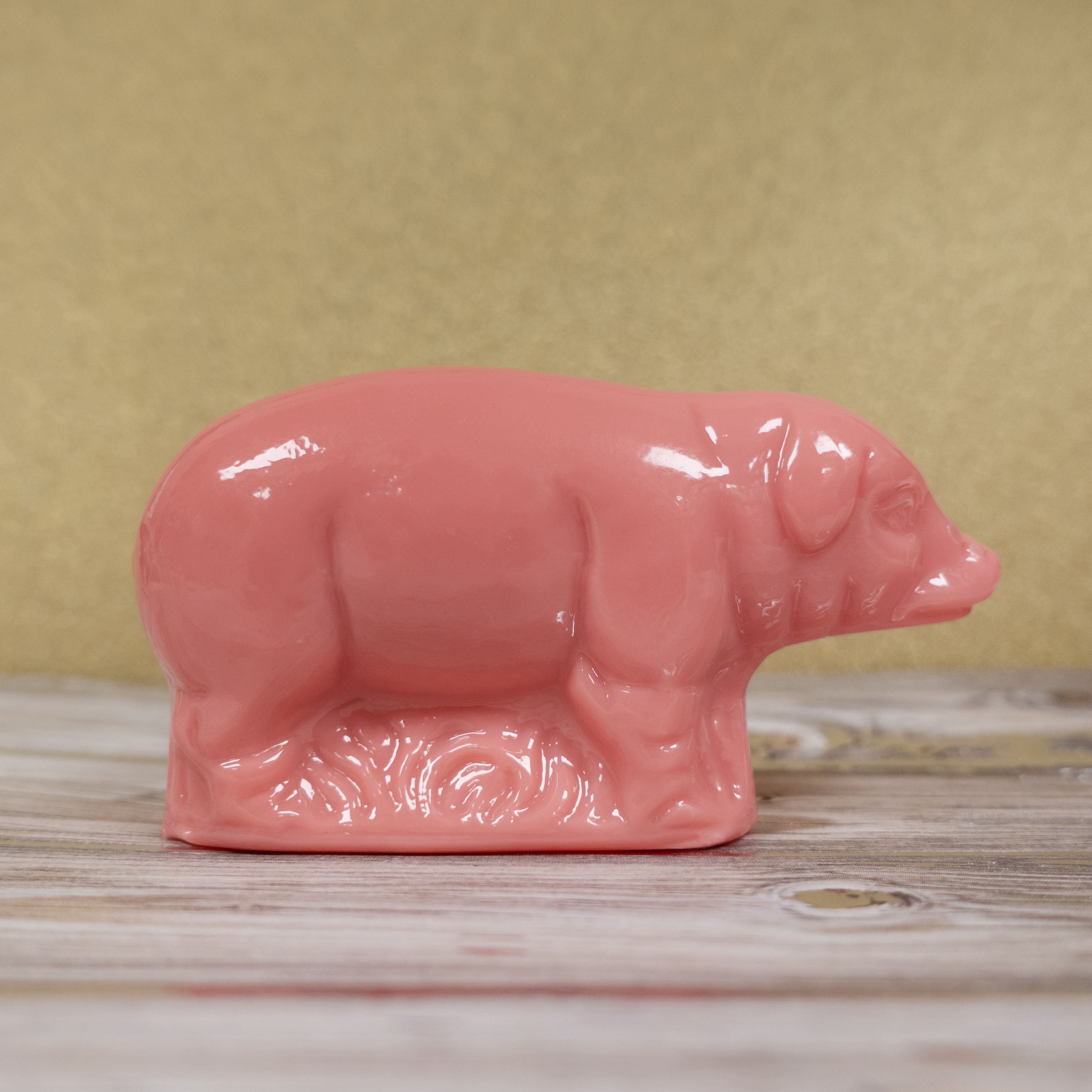 Pink hard candy pig figurine on a wooden surface with a beige background