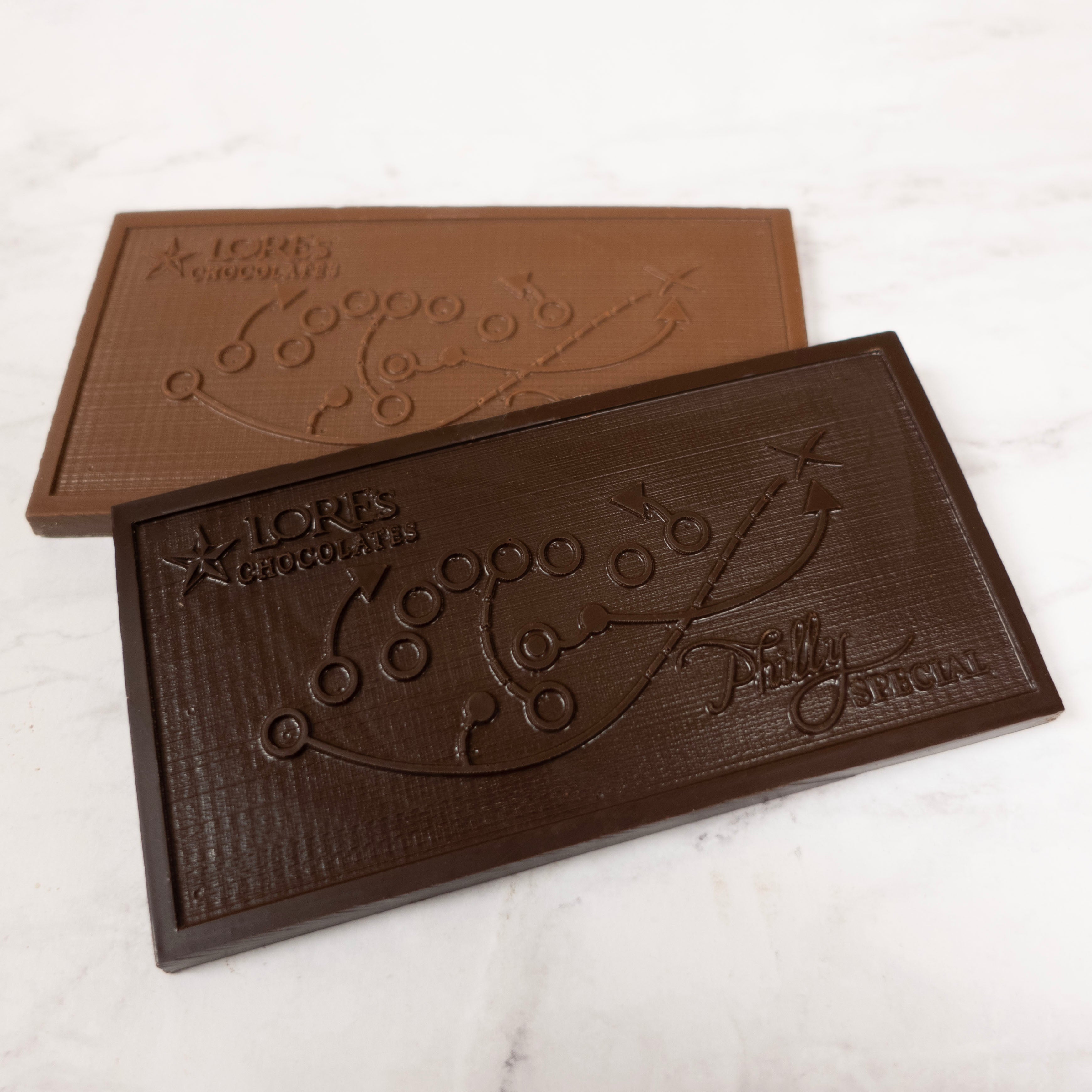 Two chocolate bars with 'Lore's Chocolates' branding and the Philly Special football play on a marble surface