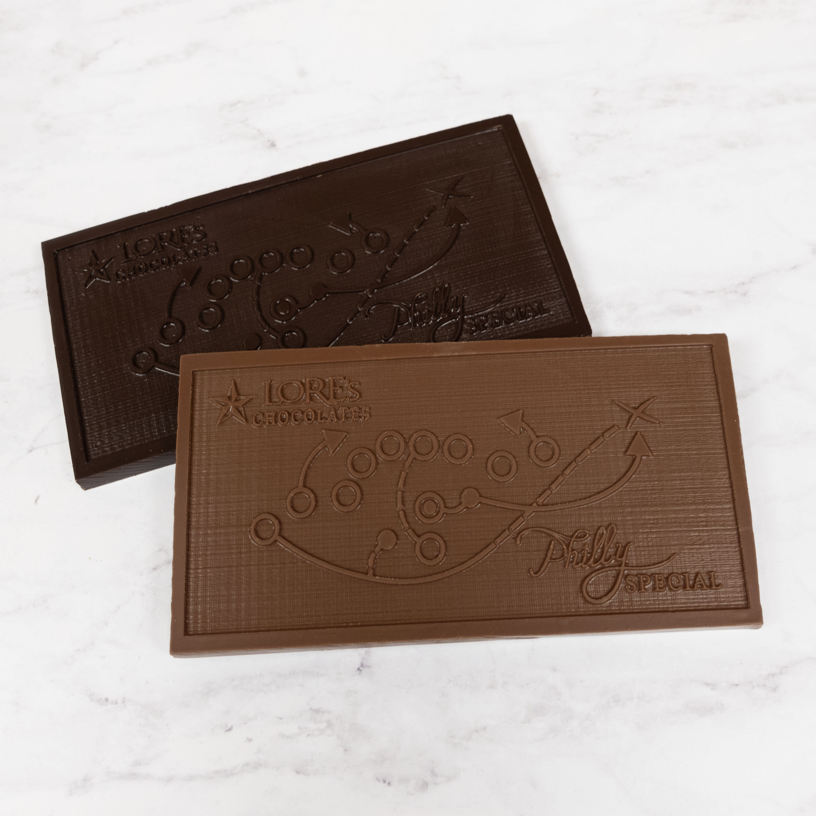 Two chocolate bars with embossed Philly Special footbal play and text on a white marble surface