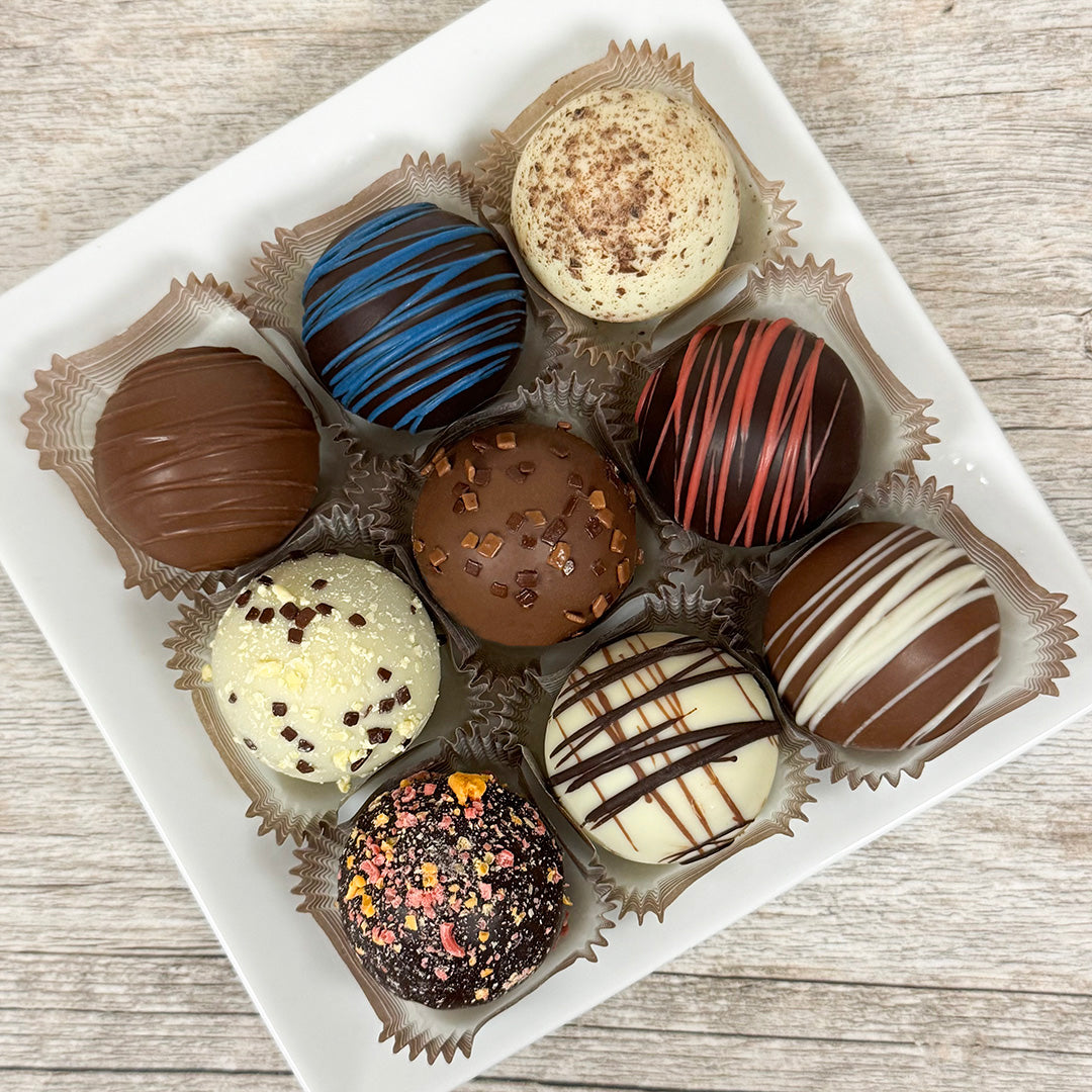 Assorted large queen-sized chocolate truffles on a white plate on a wooden surface. Sold at Lore's Chocolates in Philadelphia