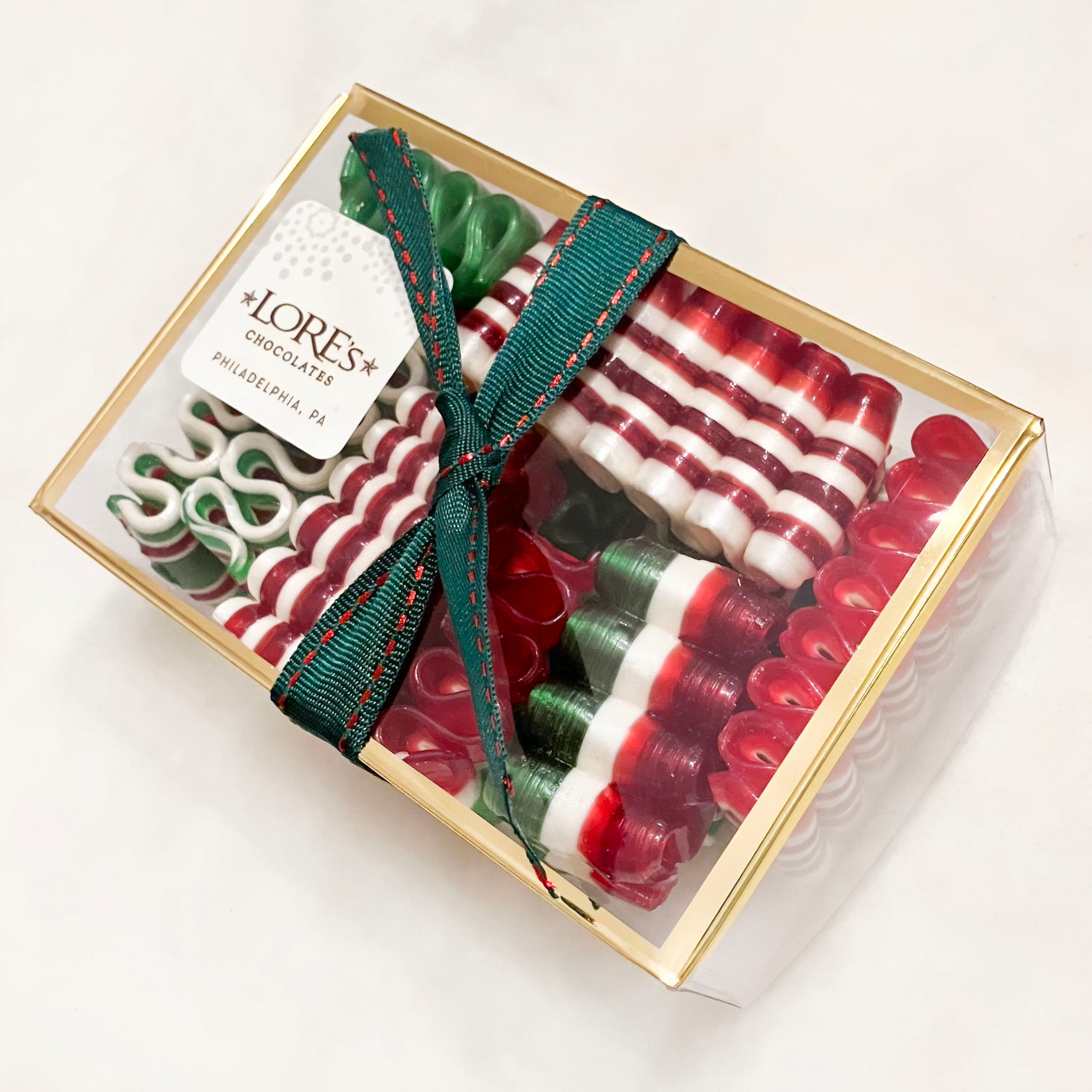Box of red and white striped ribbon candies with a green ribbon on a white background