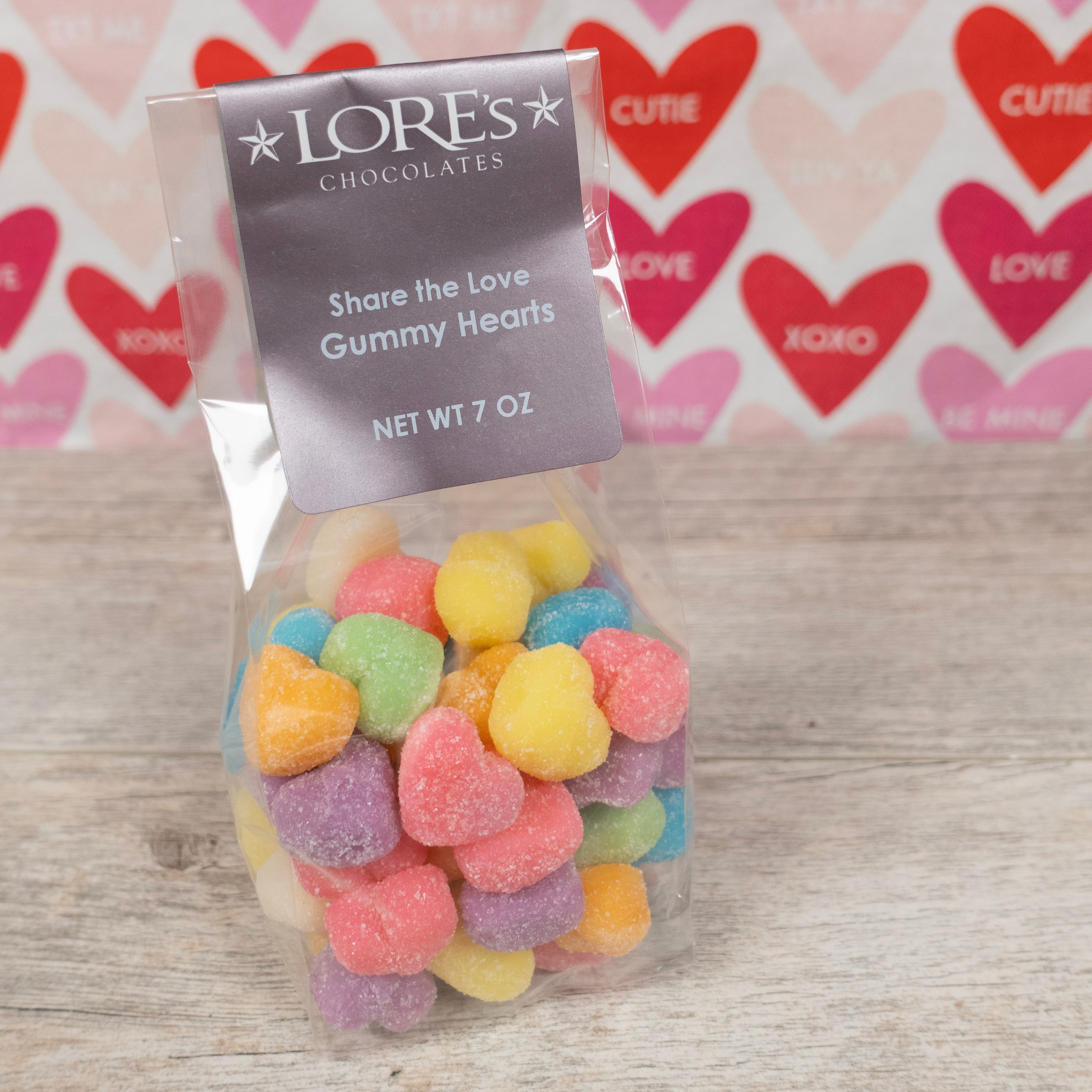 rainbow colored gummies in the shape of hearts for valentine's day pink, green, orange, purple, blue, yellow- label reads "Lore's Chocolates, Share the Love Gummy Hearts Net Wt 7 oz" 