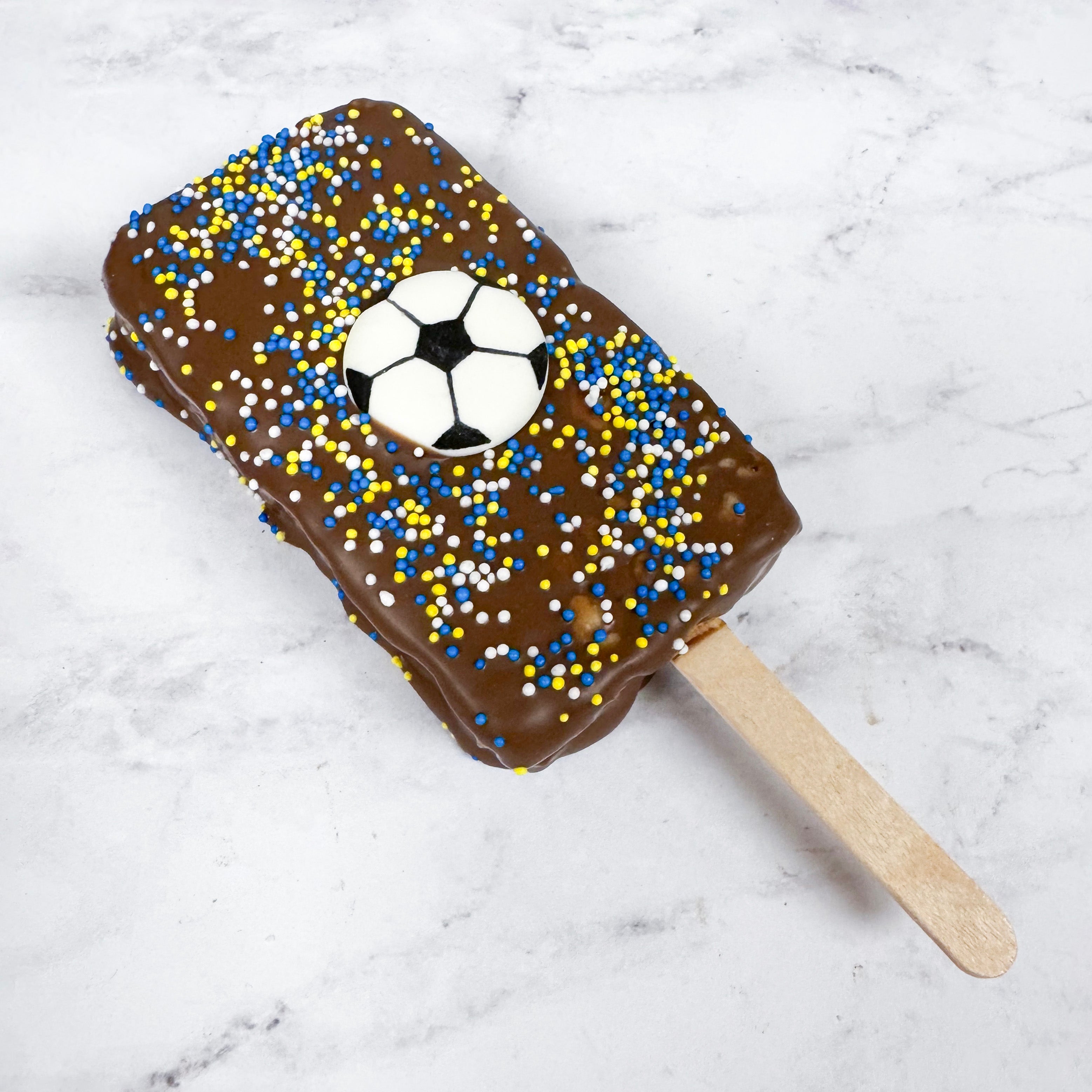 Chocolate-covered Rice Crispy Bar lollipop with a soccer ball design on a marble surface