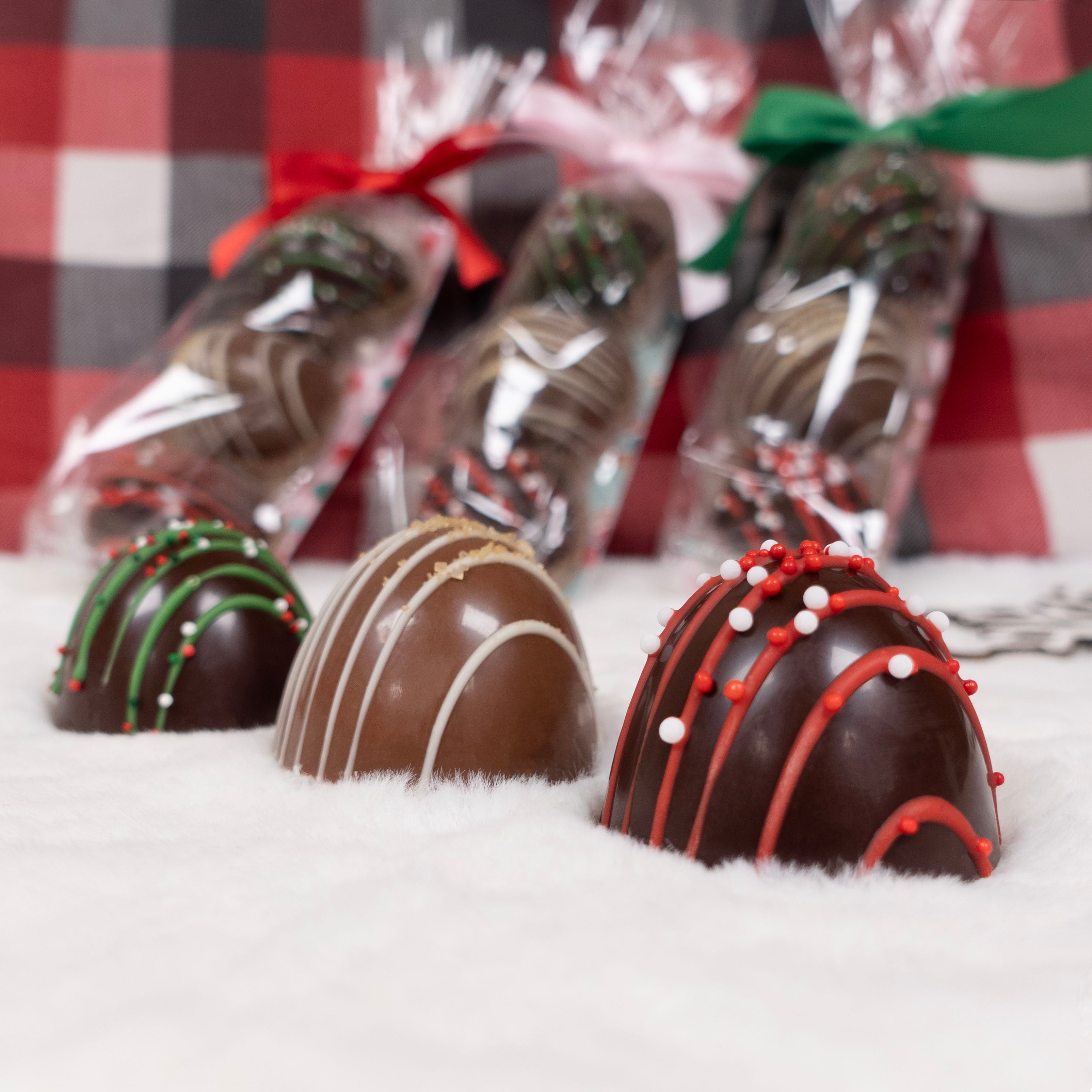 Decorative large chocolate dome truffles with festive toppings on a snowy surface, with wrapped chocolates in the background.