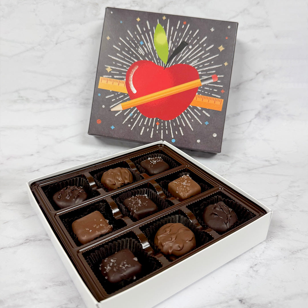 Gift Box of assorted chocolates with a decorative lid featuring an apple and pencil on a marble surface