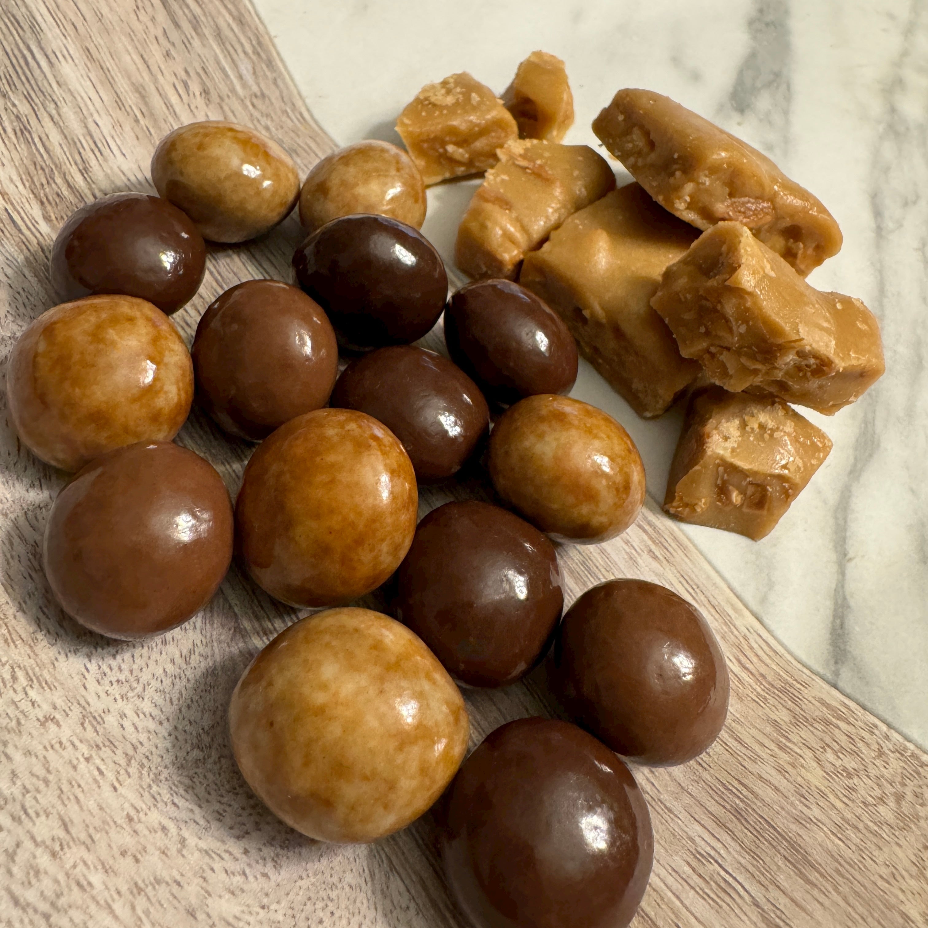 Bite-sized almond toffee bits drenched in assorted milk, dark, and white marbled chocolate displayed on a wooden surface.