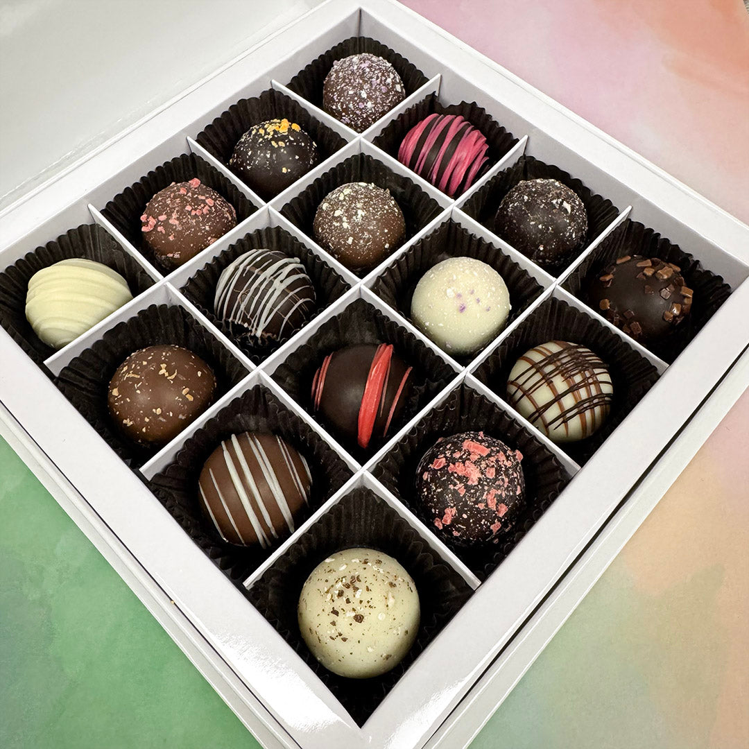 Assorted chocolate truffles in a white box on a light green surface. Sold by Lore's Chocolates in Philadelphia