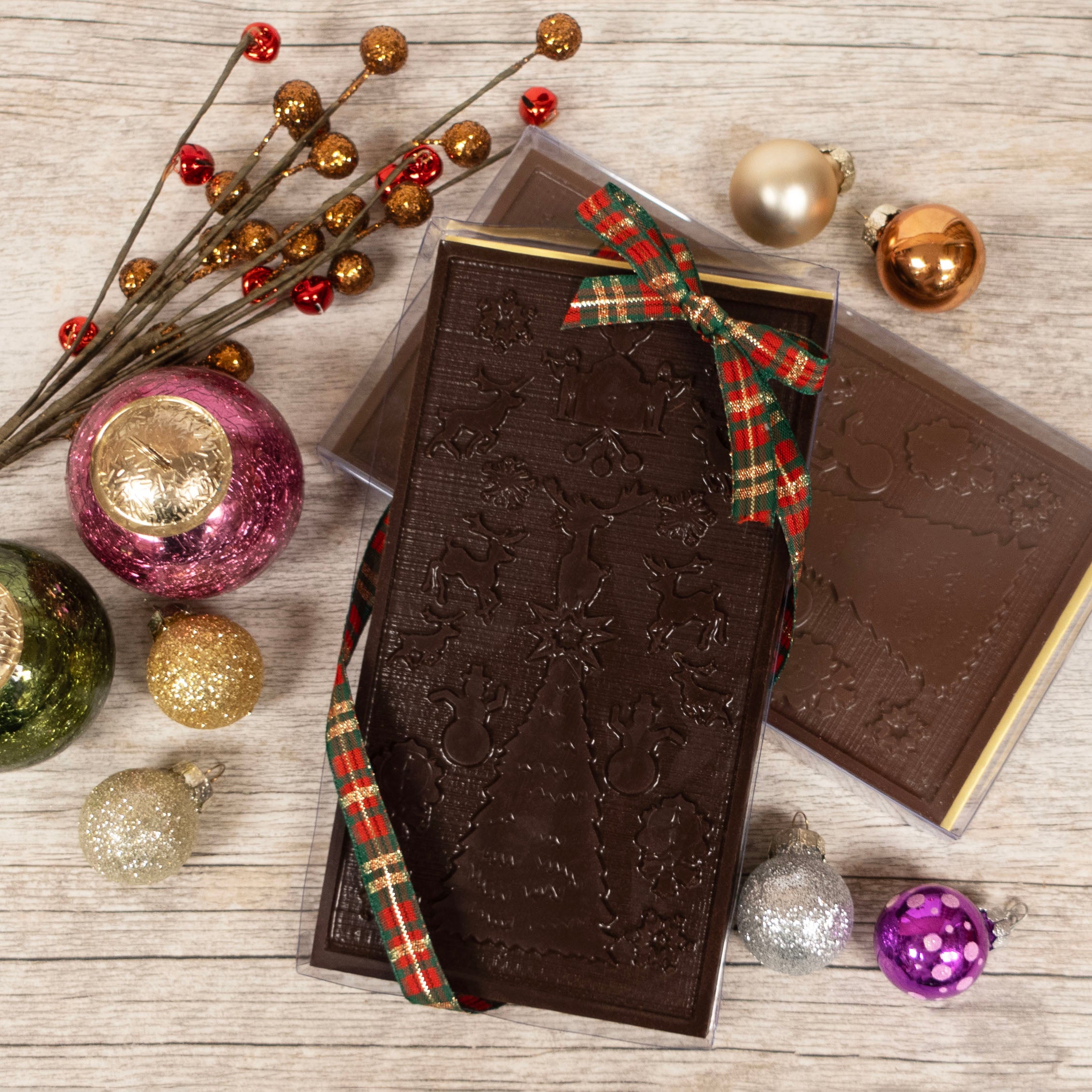 Decorative chocolate bar displaying the wanamaker light show design with a plaid ribbon on a wooden surface with Christmas ornaments.