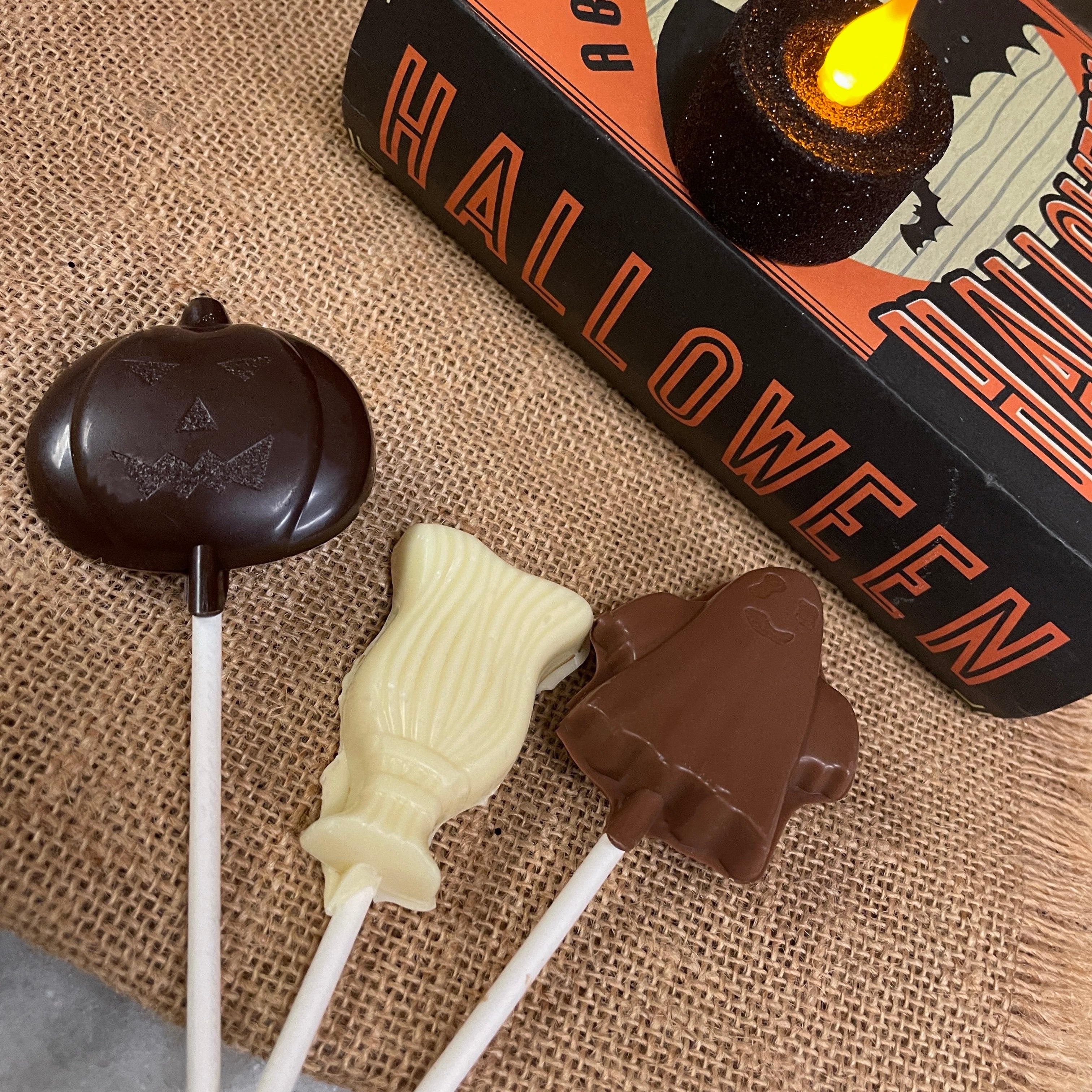 Three chocolate lollipops - dark chocolate jack-o-lantern pumpkin, white chocolate witch's broom, and milk chocolate ghost